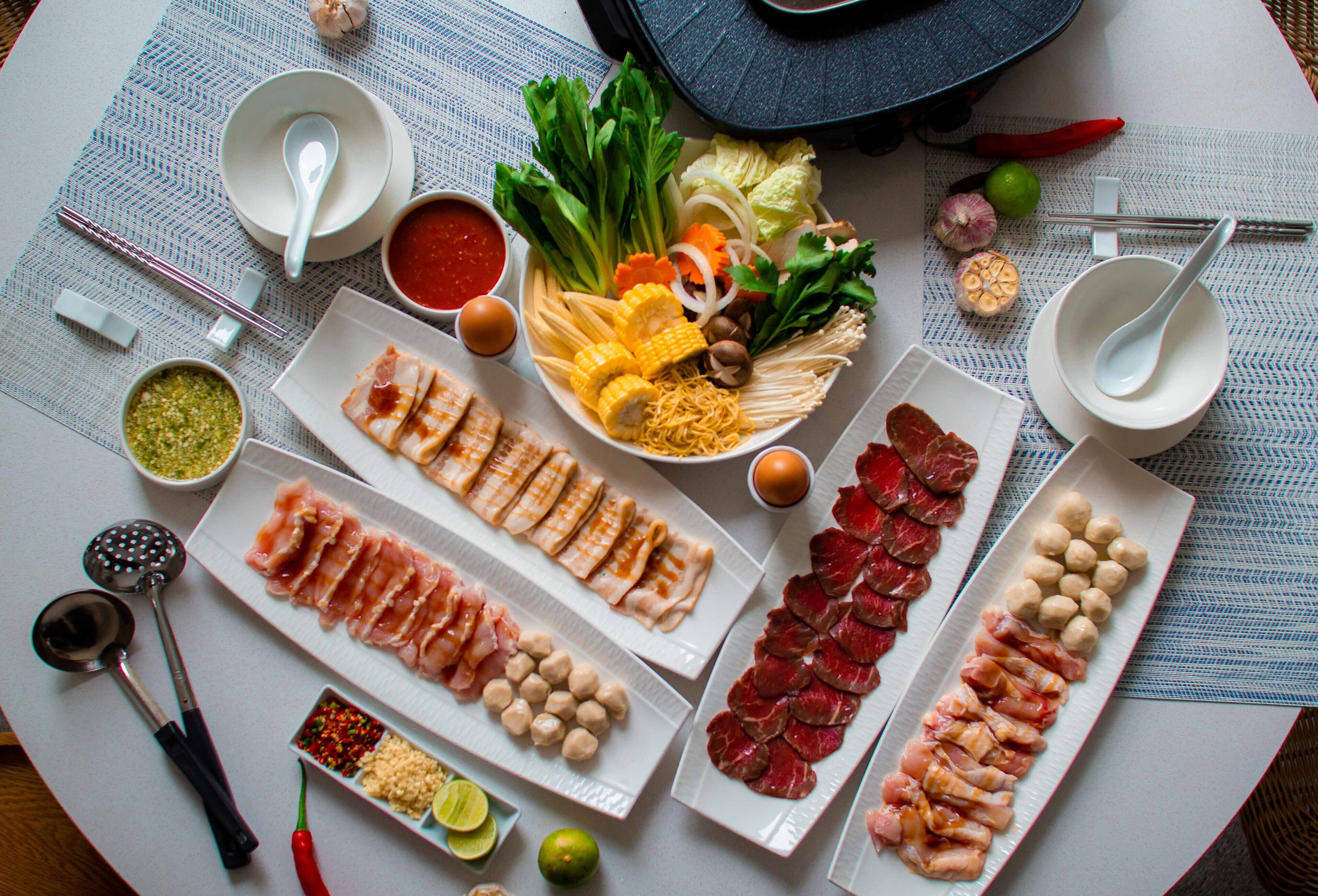 Una mesa con diversos alimentos, como carnes, verduras y salsas, dispuesta para una comida.