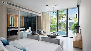 A modern hotel room with a large bed, a sitting area, a dining table, and a view of the pool. - Oceanphere Pattaya Villa (Sattahip)