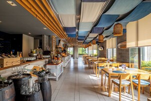 A restaurant interior with wooden tables and chairs, a bar area with bottles and glasses, and a view through large windows.