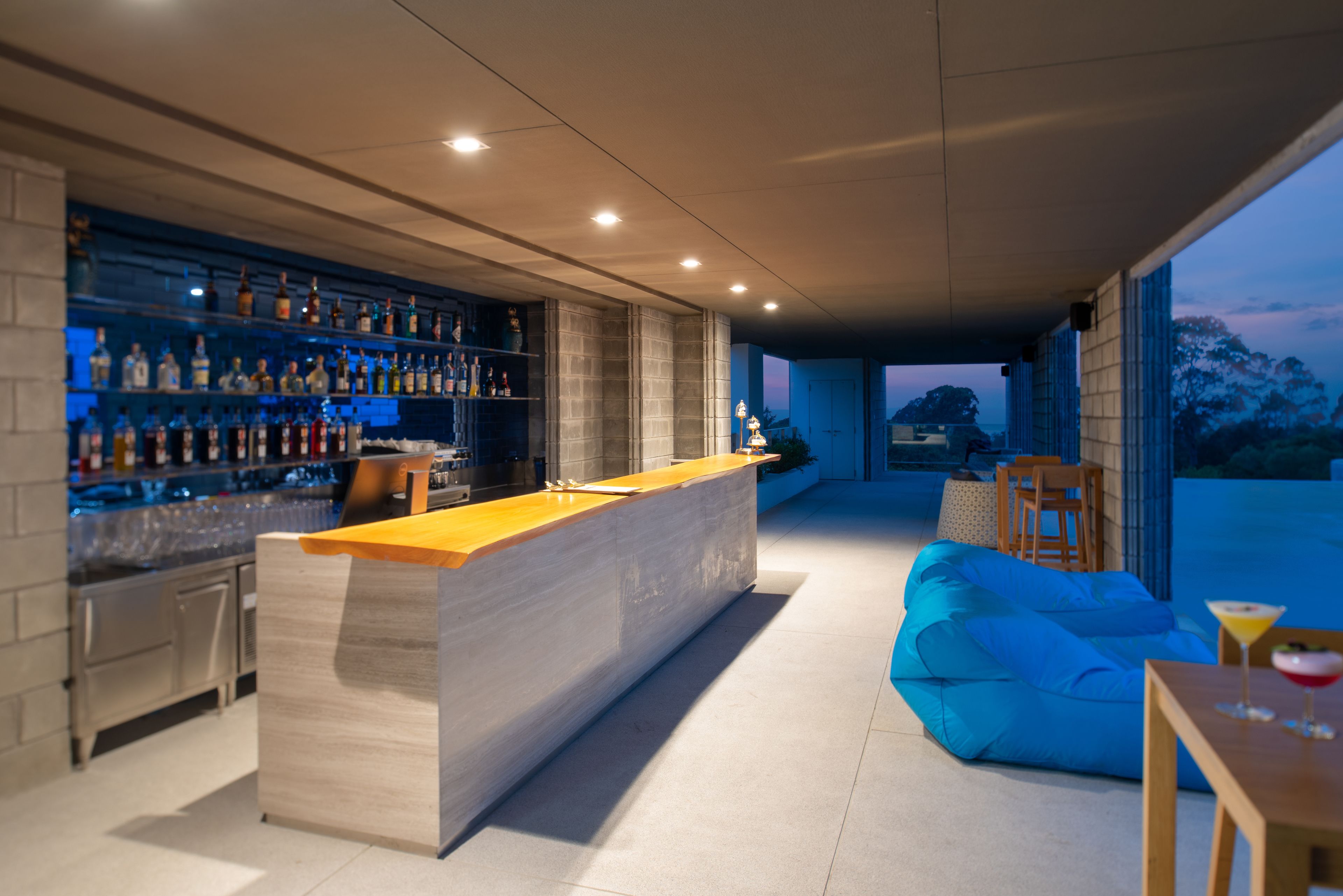A modern bar area with a long counter, shelves of bottles, and a blue seating area.