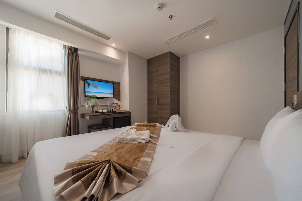 A modern hotel room with a large bed, a desk with a computer, a TV, and a view of the ocean.