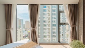 A modern hotel room with a large window, a bed, and a view of high-rise buildings. - Zenia Boutique Hotel Nha Trang (Nha Trang)