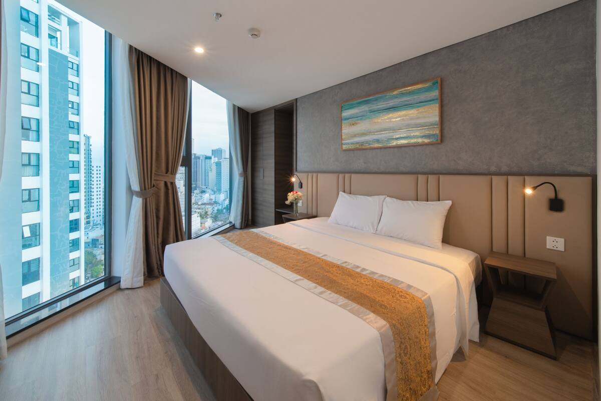 A modern hotel room with a large bed, a view of the city, and a painting on the wall.