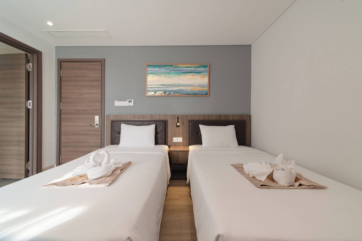 A hotel room with two beds, a painting on the wall, and a wooden floor.