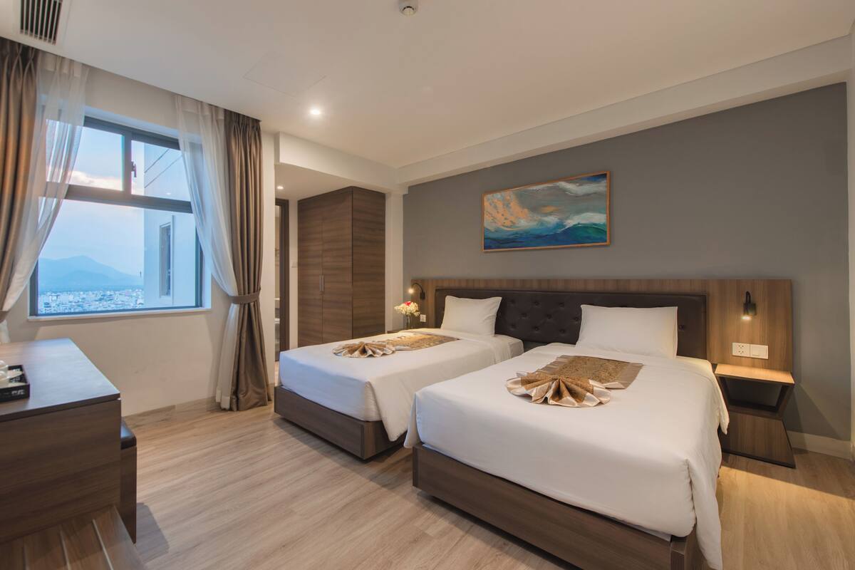 A hotel room with two beds, a desk, a chair, a telephone, and a painting on the wall.