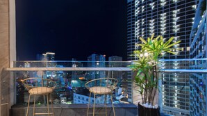 A balcony with two wicker chairs, a potted plant, and a cityscape view at night. - Zenia Boutique Hotel Nha Trang (Nha Trang)