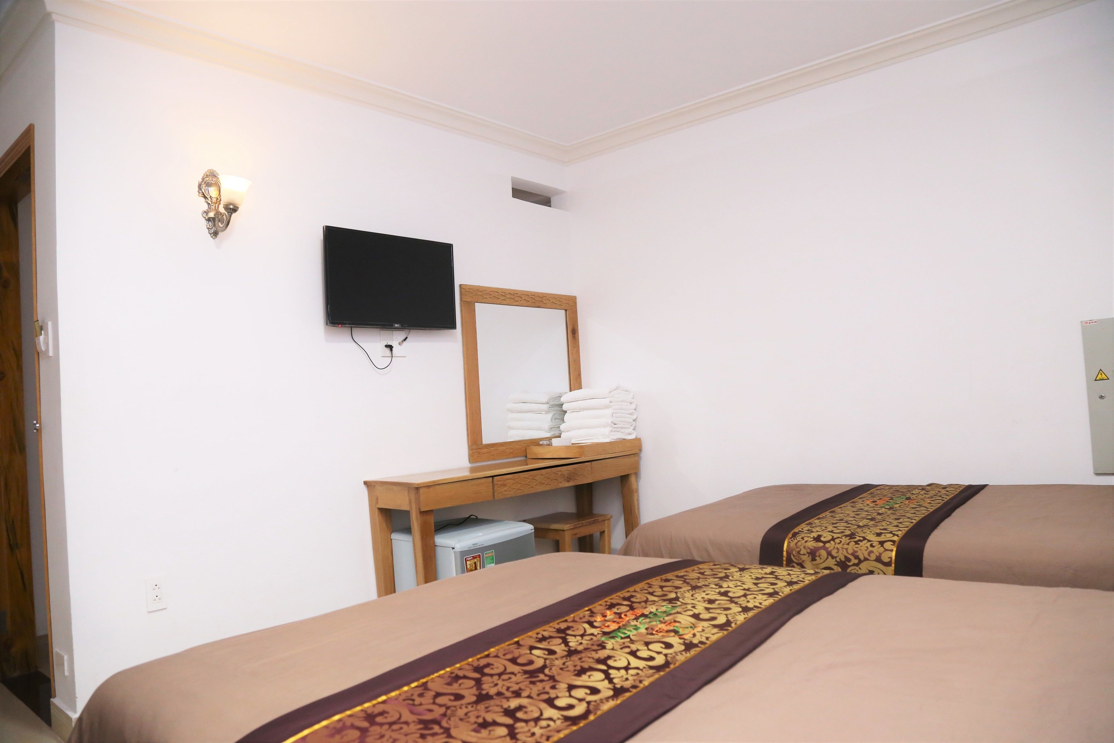 A hotel room with two beds, a television, a mirror, a small table with towels, and a wardrobe.