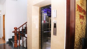 A hotel lobby with a marble staircase, an elevator, and a reception area with a decorative wall. - Da Lat Phu Tho Hotel (Xuan Huong - Da Lat)