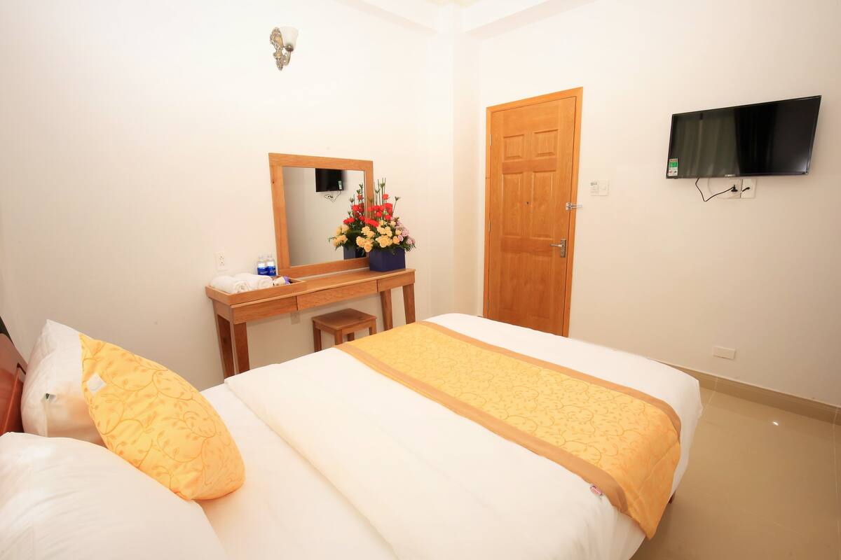 A hotel room with a bed, a wooden dresser, a mirror, a TV, and a door.