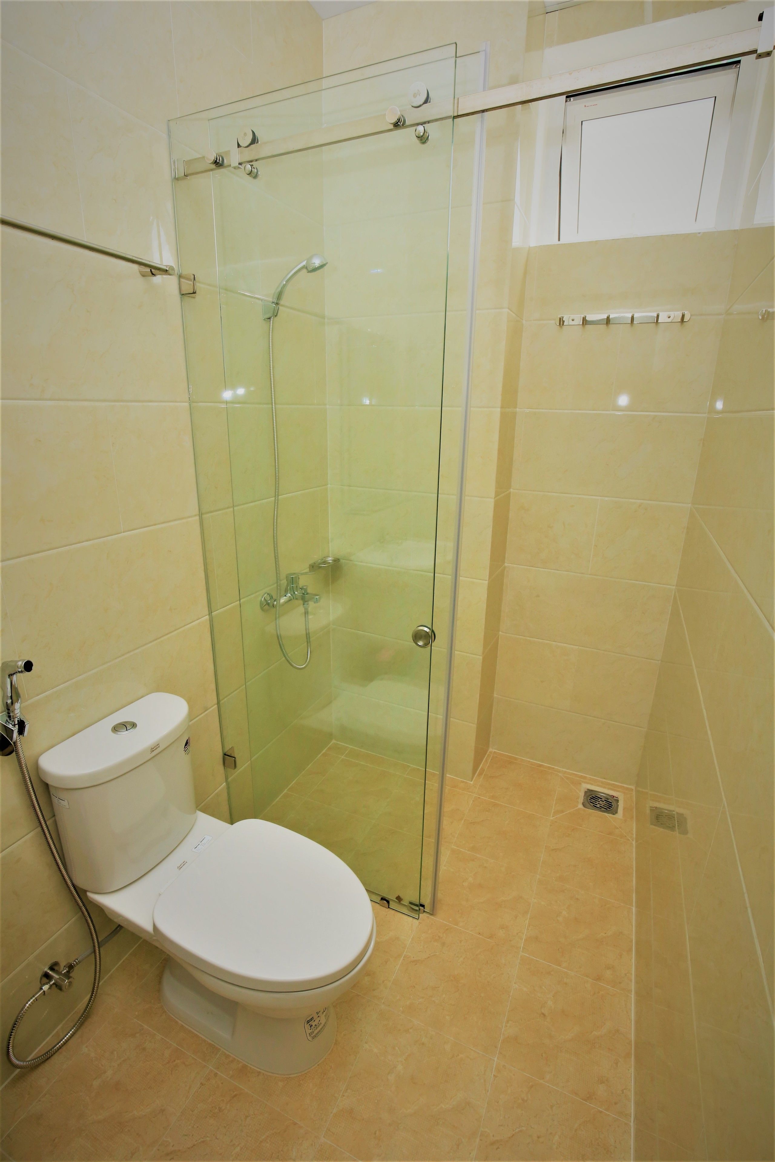 A bathroom with a glass-enclosed shower, a toilet, and beige tiled walls.