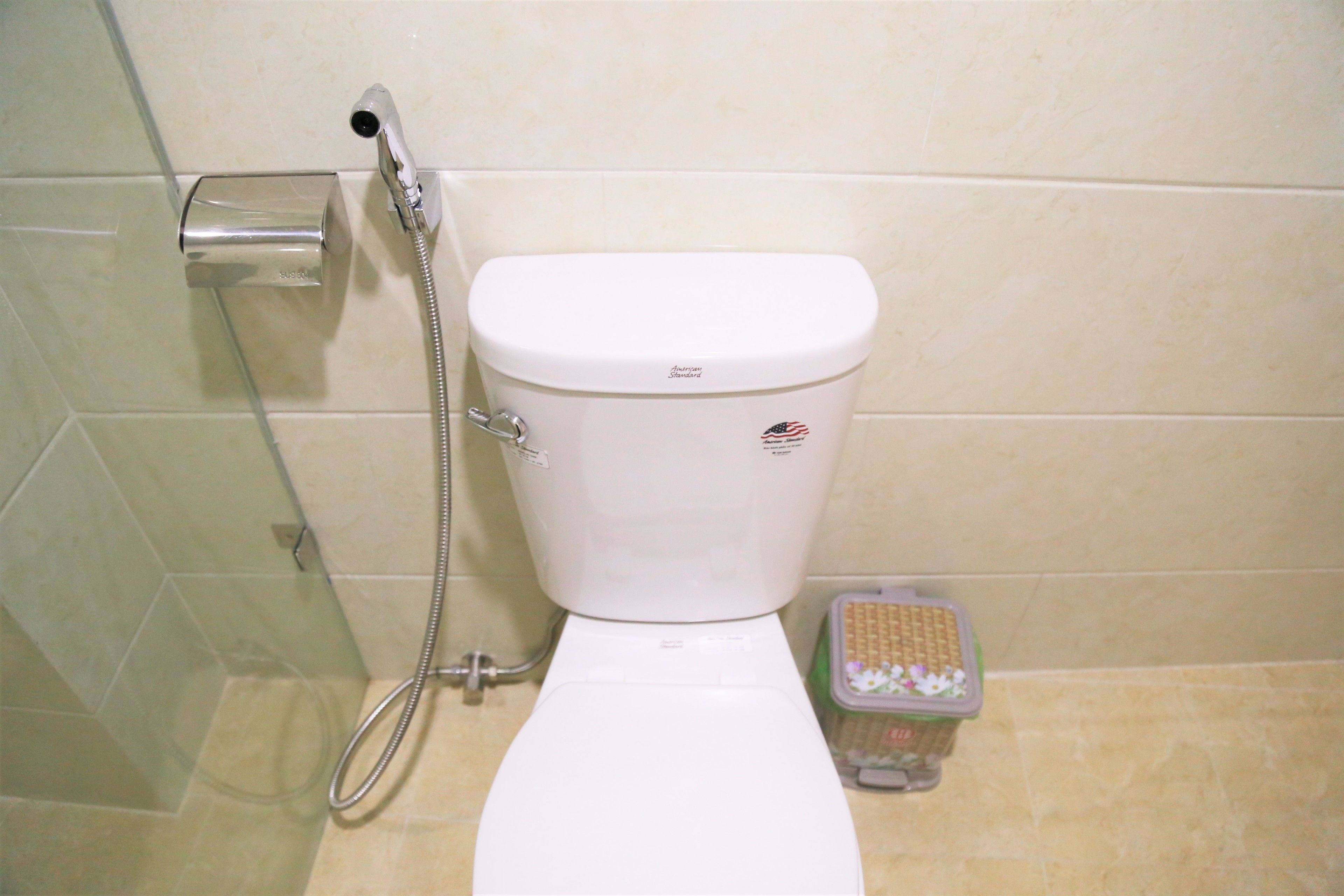 A bathroom with a toilet, a shower, and a trash bin.