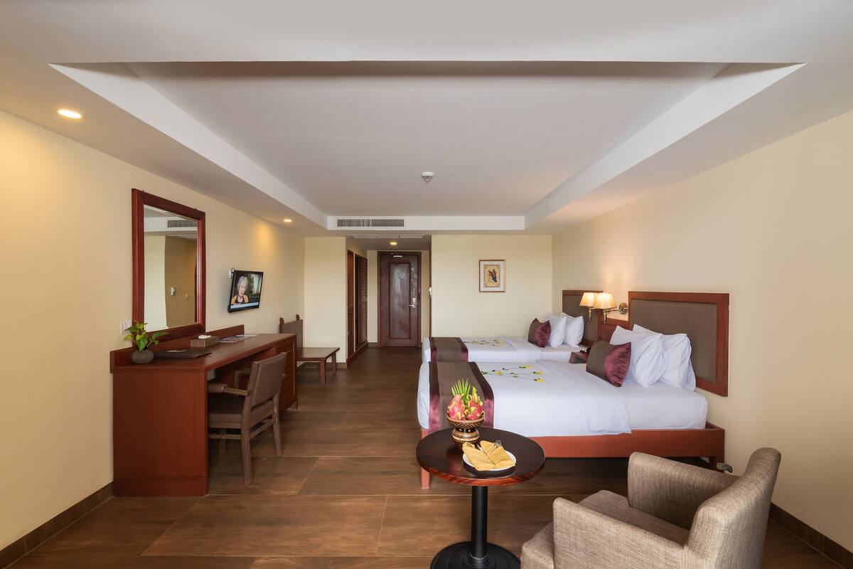 Quarto de hotel com cama, escrivaninha, cadeira, uma mesinha com uma fruteira e um espelho.