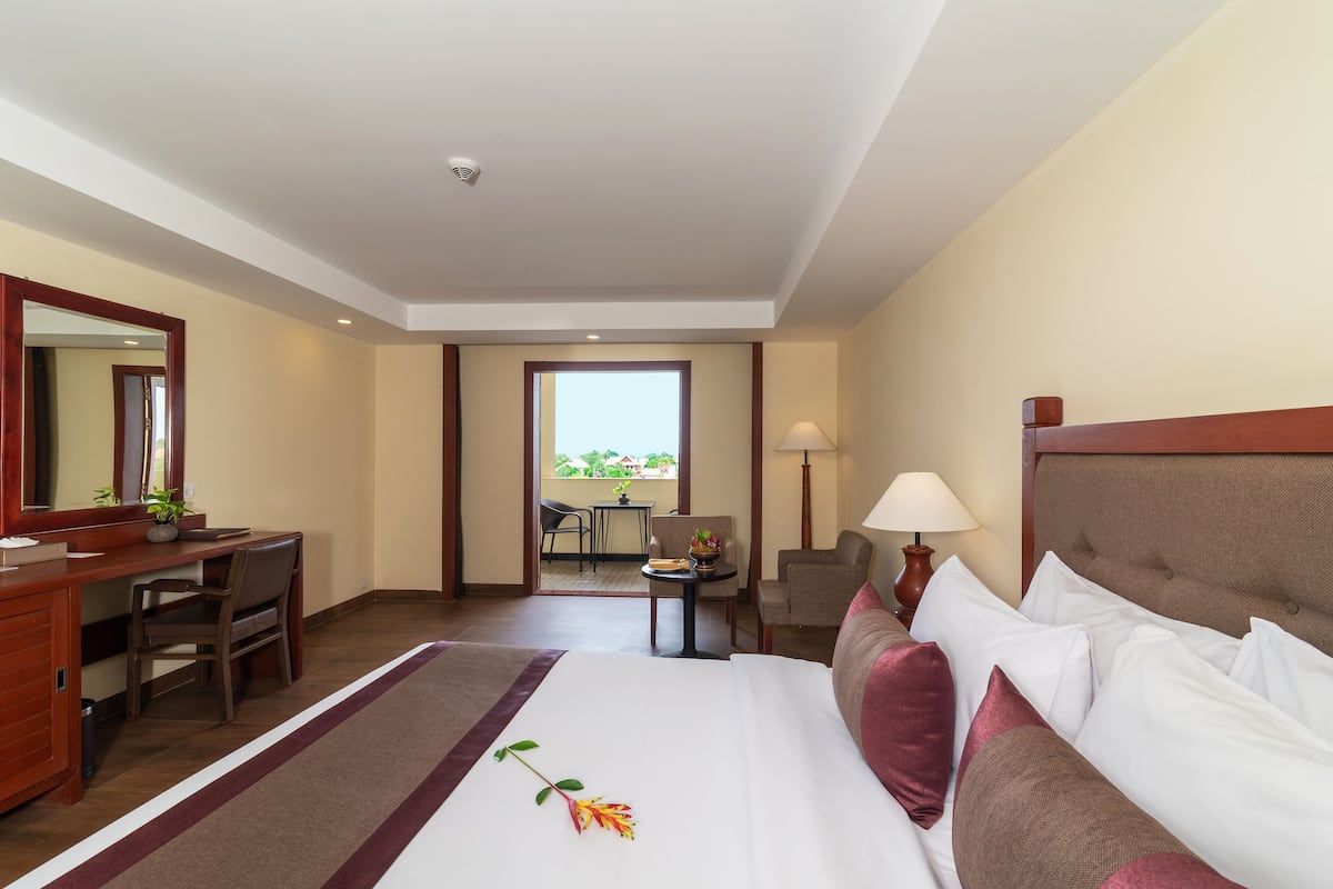 Quarto de hotel com cama, escrivaninha, cadeira, luminária e vista para o exterior.