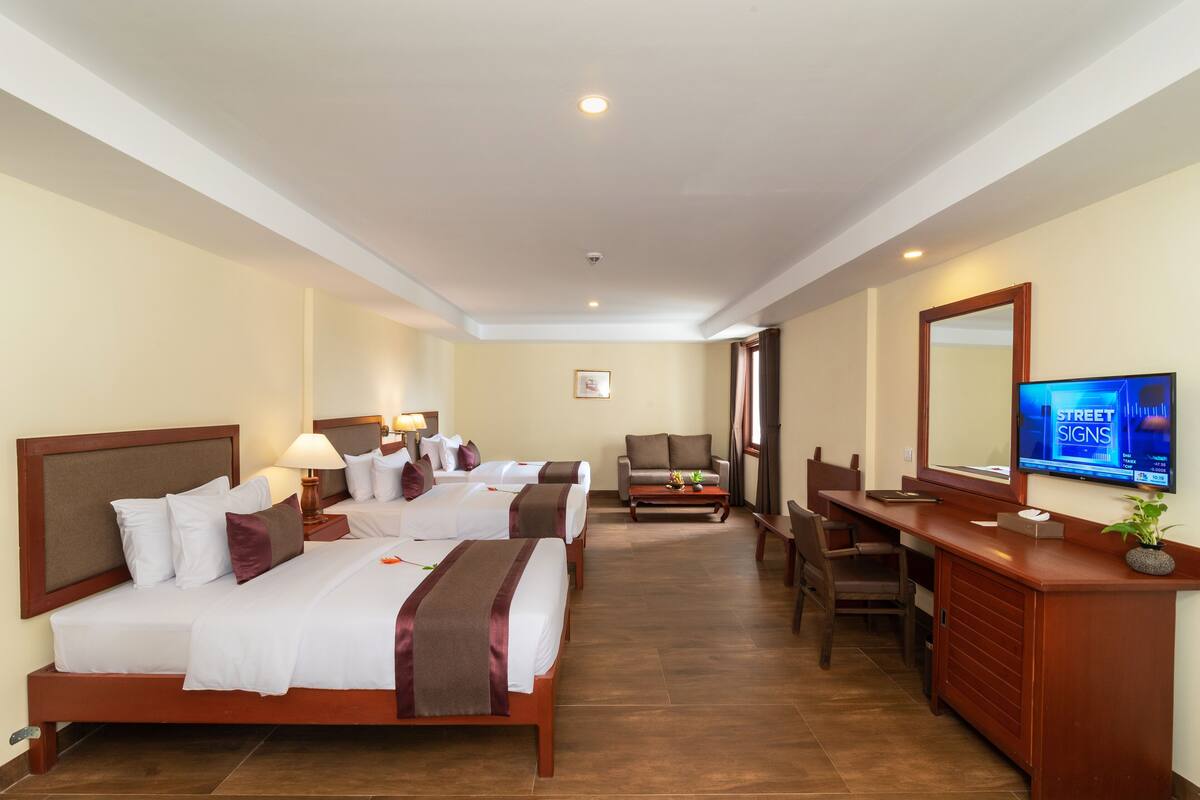 Quarto de hotel com duas camas, uma escrivaninha, uma cadeira, uma televisão e uma pequena planta.