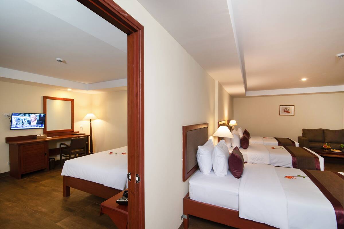 Quarto de hotel com duas camas, uma escrivaninha com cadeira, televisão e sofá.