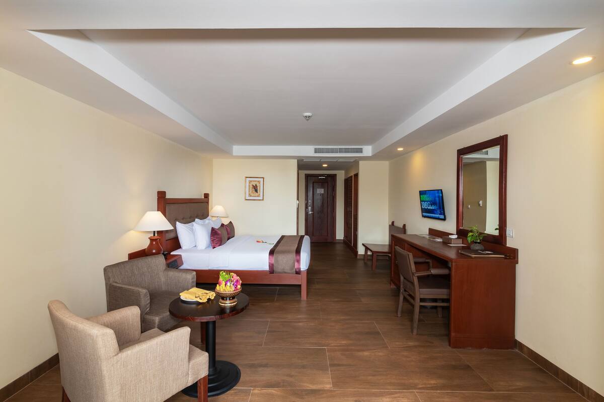 Quarto de hotel com cama, escrivaninha, cadeira e televisão.