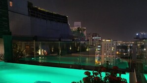 Una piscina en la azotea con barandilla de cristal, rodeada de follaje y flores.