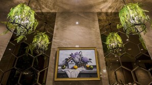 Una obra de arte enmarco que muestra una casa con flores y frutas, rodeada de espejos hexagonales y plantas verdes colgantes.