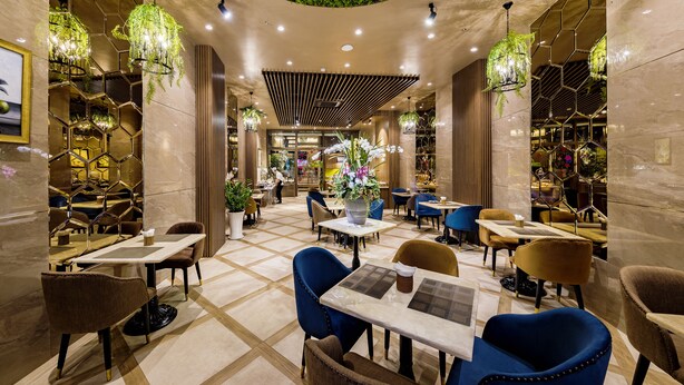 Un interior moderno con lámparas hexagonales, un área de estar central con mesas y sillas, y una pared verde en la parte superior.