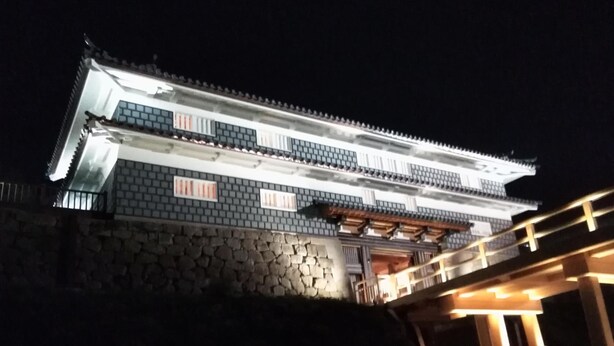 En traditionell japansk byggnad med en grund av sten och flera våningar, upplyst på natten.