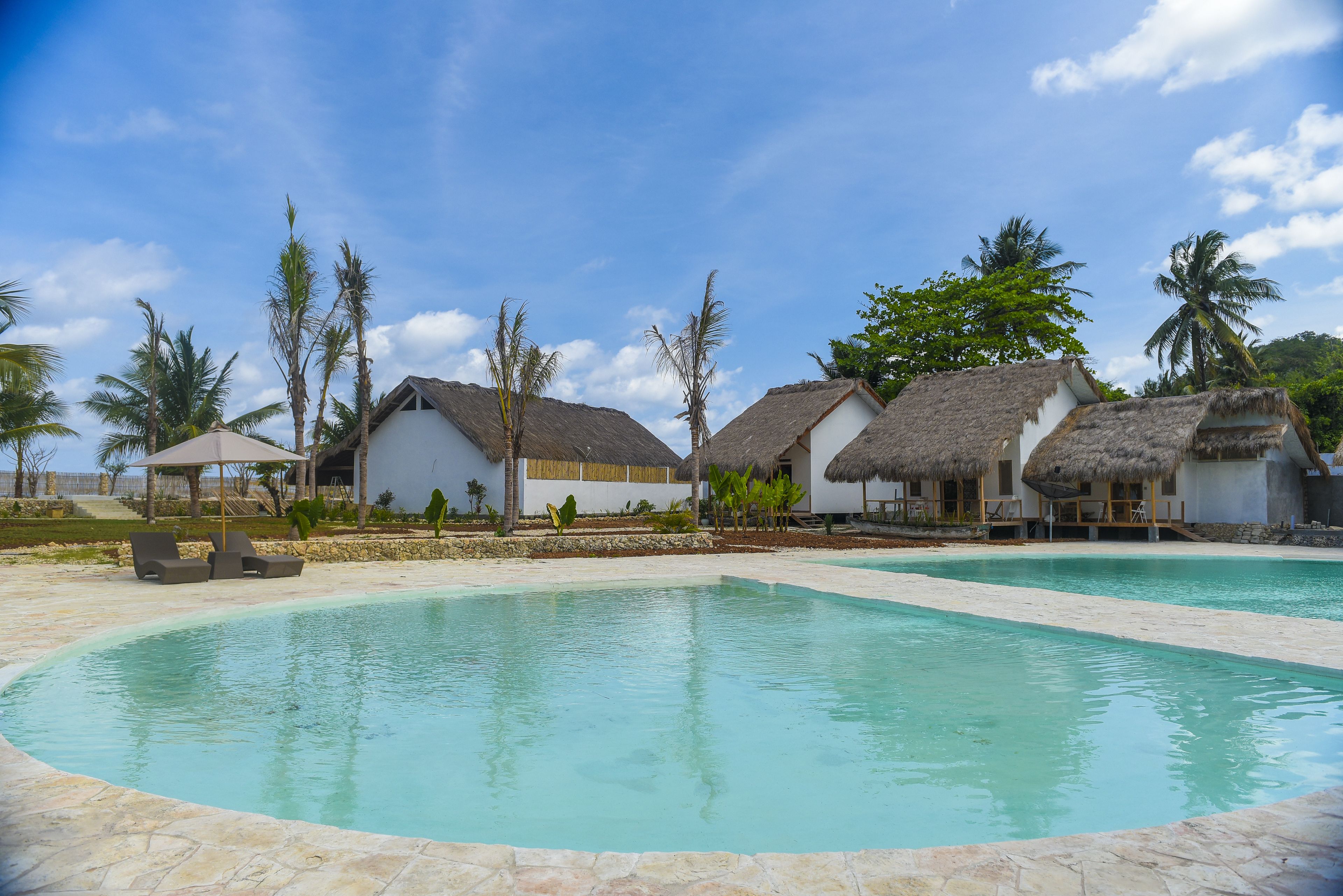 A pool area with thatched-roof huts and palm trees.
