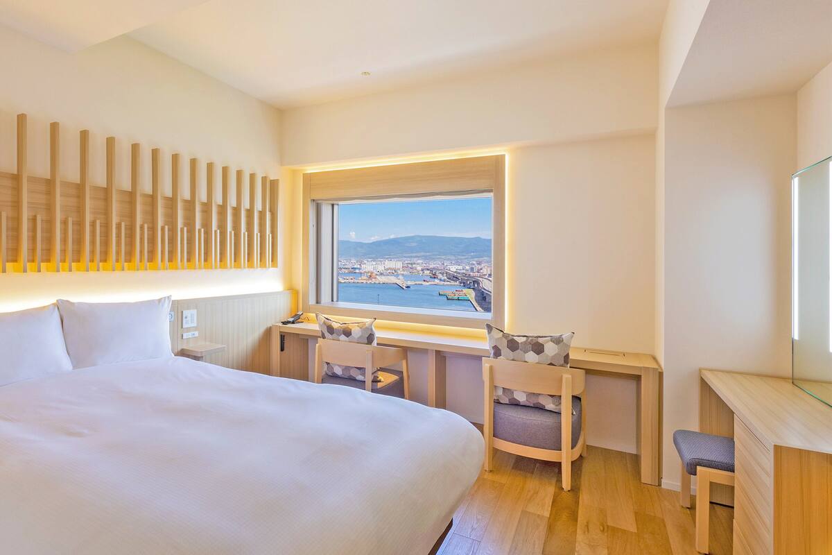 Une chambre d’hôtel avec un grand lit, un bureau avec une chaise, une vue sur le paysage urbain et un panneau mural en bois.