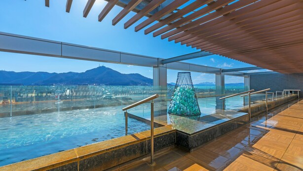 Ein von Glas umgebener Infinity-Pool mit freiem Blick auf das Meer und die dahinter liegenden Berge.