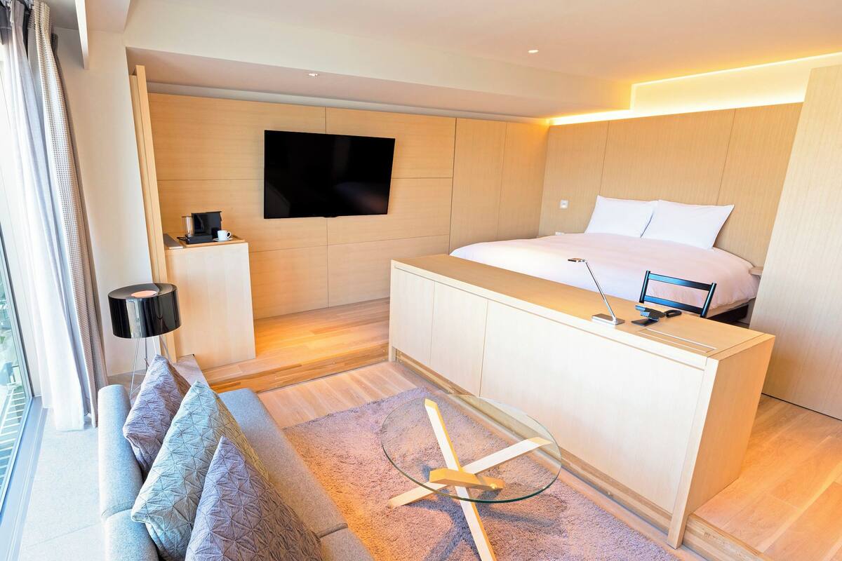 Une chambre d’hôtel moderne dotée d’une grande fenêtre, d’un lit, d’un bureau et d’un téléviseur à écran plat.