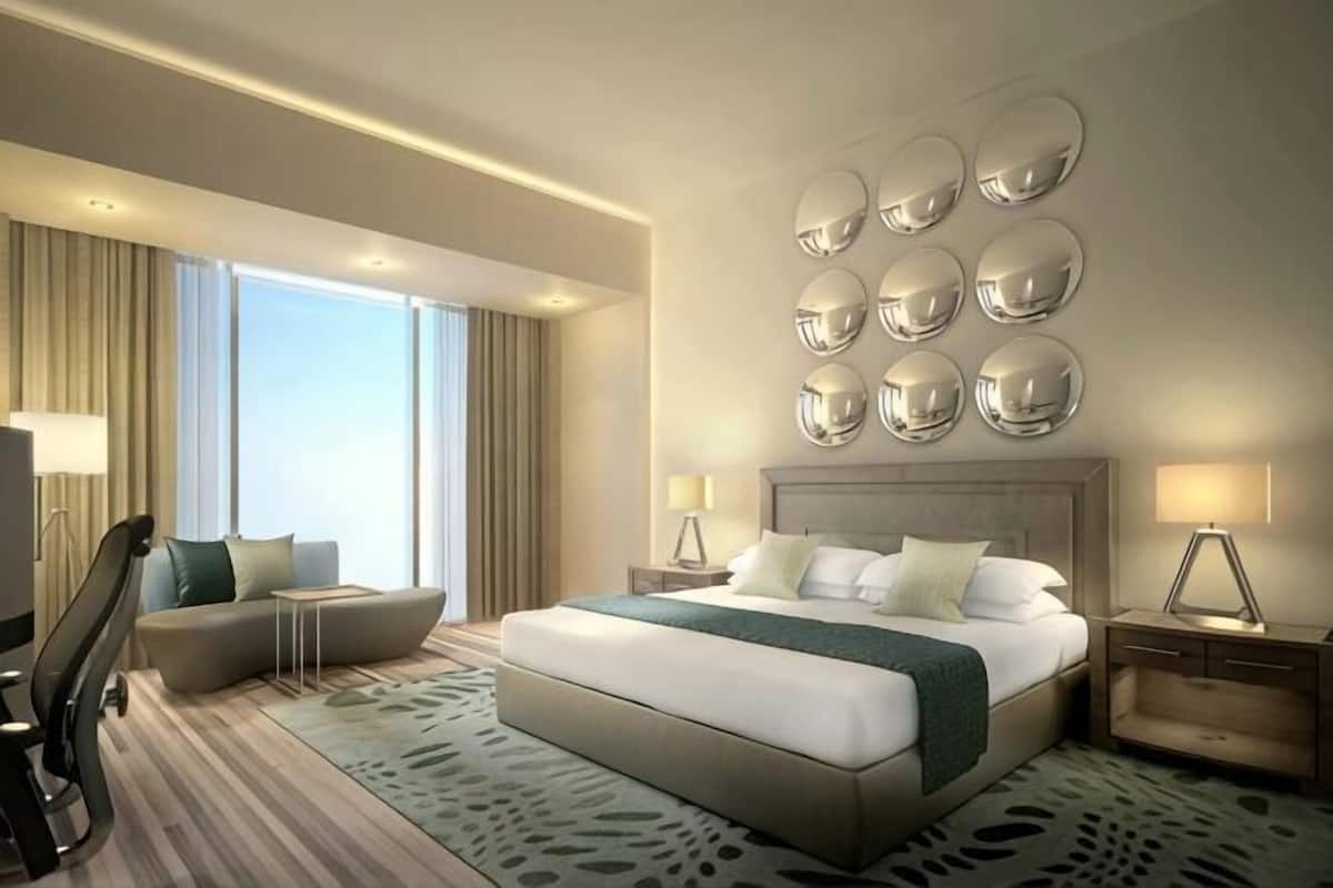 A modern hotel room with a large bed, a seating area, and a view of the outdoors.
