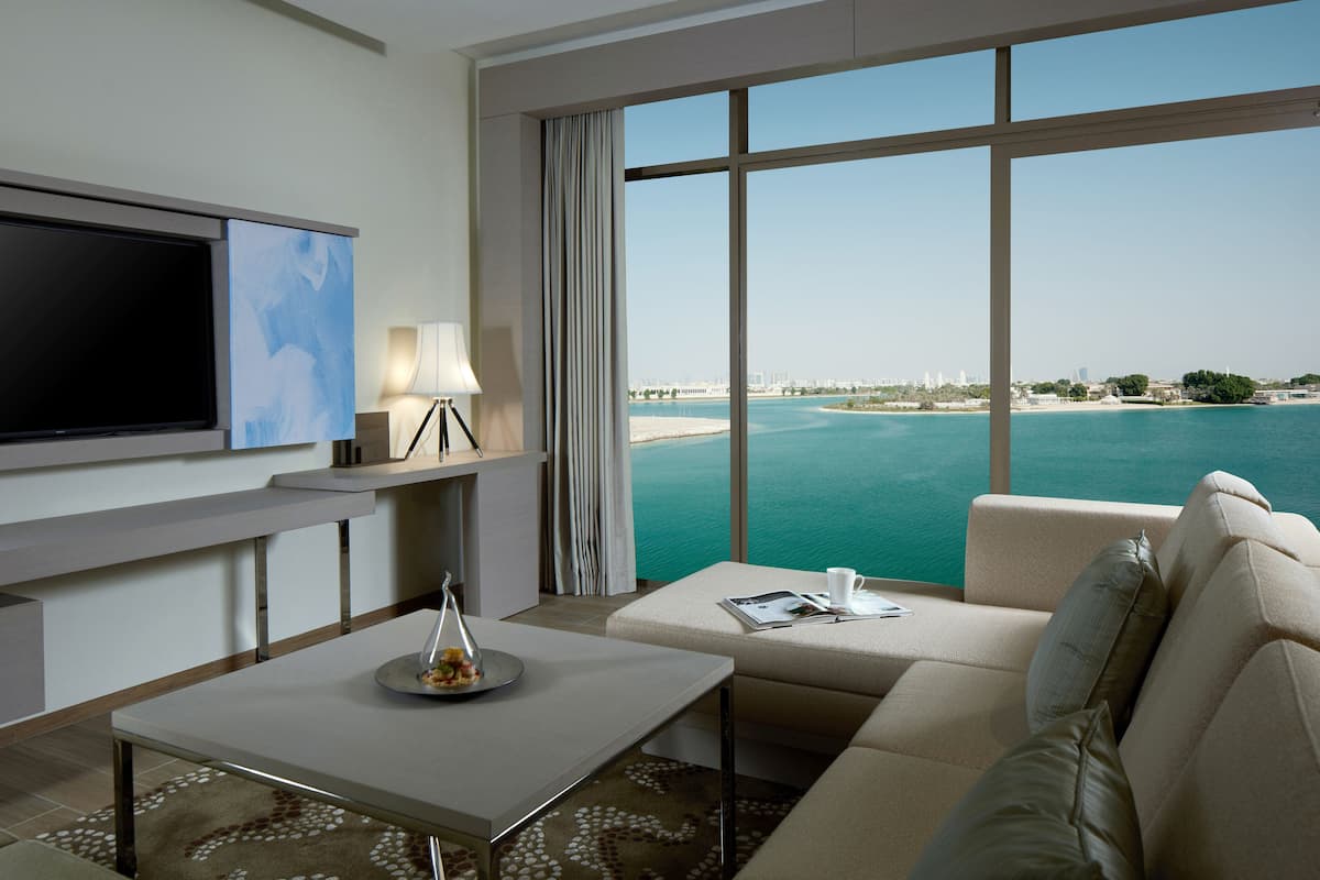 A modern hotel room with a large window offering a view of the sea and cityscape.