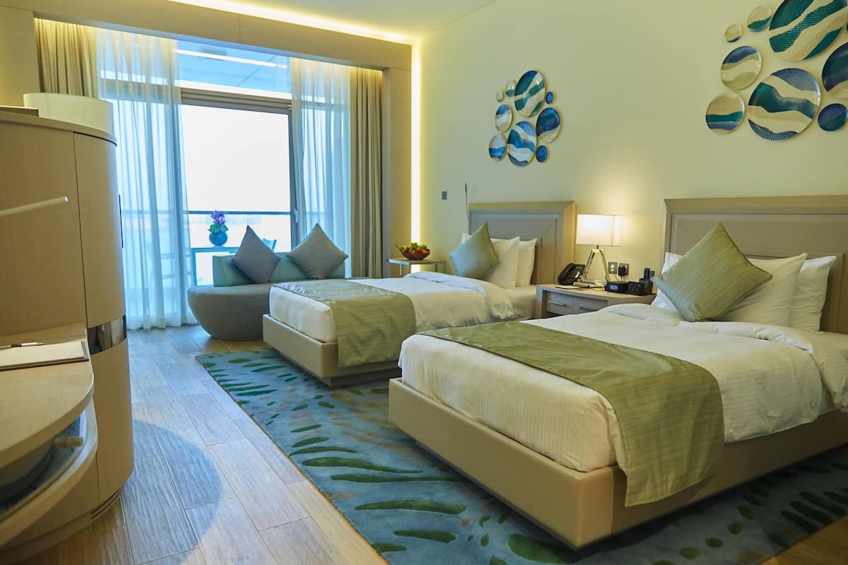 A hotel room with two beds, a sofa, a desk, and a view of the outdoors.