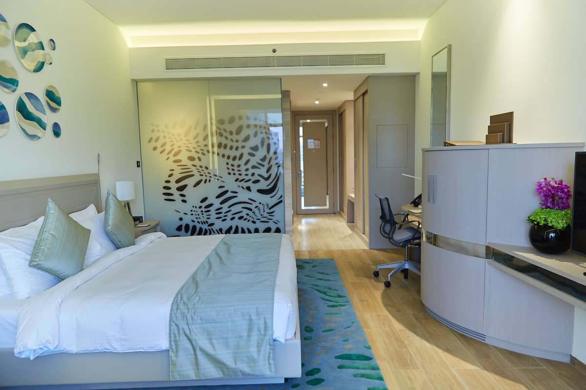 A modern hotel room with a large bed, a desk, a wardrobe, and a decorative wall.