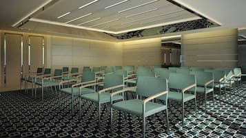 A conference room with rows of green chairs, a patterned carpet, and a ceiling with linear lighting fixtures.
