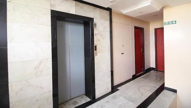 A hallway with marble flooring, a central elevator, and red doors. - Hotel Naveen (Coimbatore)
