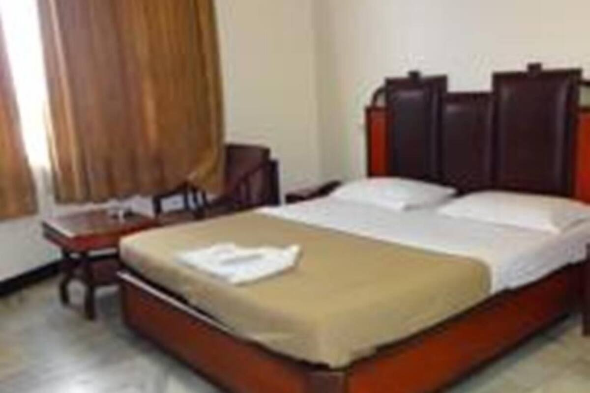 Une chambre d’hôtel standard, avec un lit simple, une tête de lit en bois, une petite table de chevet et une chaise.