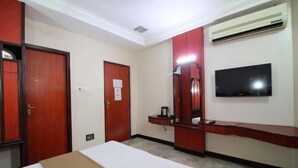 A hotel room with a bed, a desk, a mirror, a television, and an air conditioning unit. - Hotel Naveen (Coimbatore)