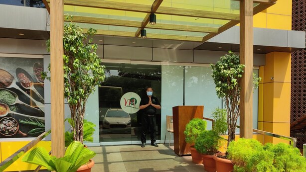 A modern building entrance with a glass door, potted plants, and a wooden structure. - Metro Plaza Hotel (Mangaluru)