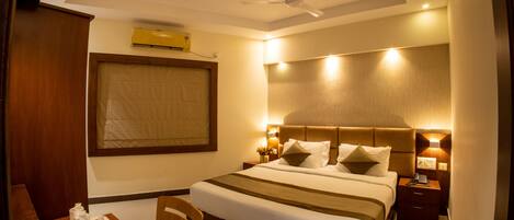 A hotel room with a large bed, a desk with a chair, a ceiling fan, and a nightstand with a lamp.