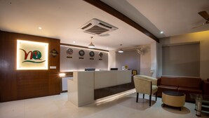 A hotel reception area with a modern design, featuring a reception desk, a seating area with a sofa and chairs, and a wall with clocks and a logo. - Metro Plaza Hotel (Mangaluru)