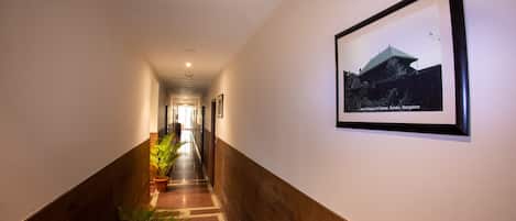 Un pasillo con un cuadro enmarcado de un edificio, plantas en macetas y suelo de madera.