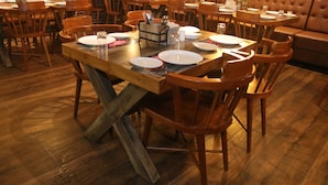 A restaurant with wooden tables and chairs, a brick wall, and a leather booth. - Metro Plaza Hotel (Mangaluru)