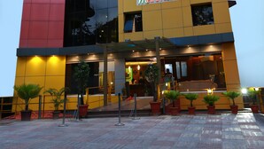 A modern hotel with a red and yellow facade, a prominent sign reading "Metro Plaza Hotel," and a well-lit entrance with potted plants. - Metro Plaza Hotel (Mangaluru)