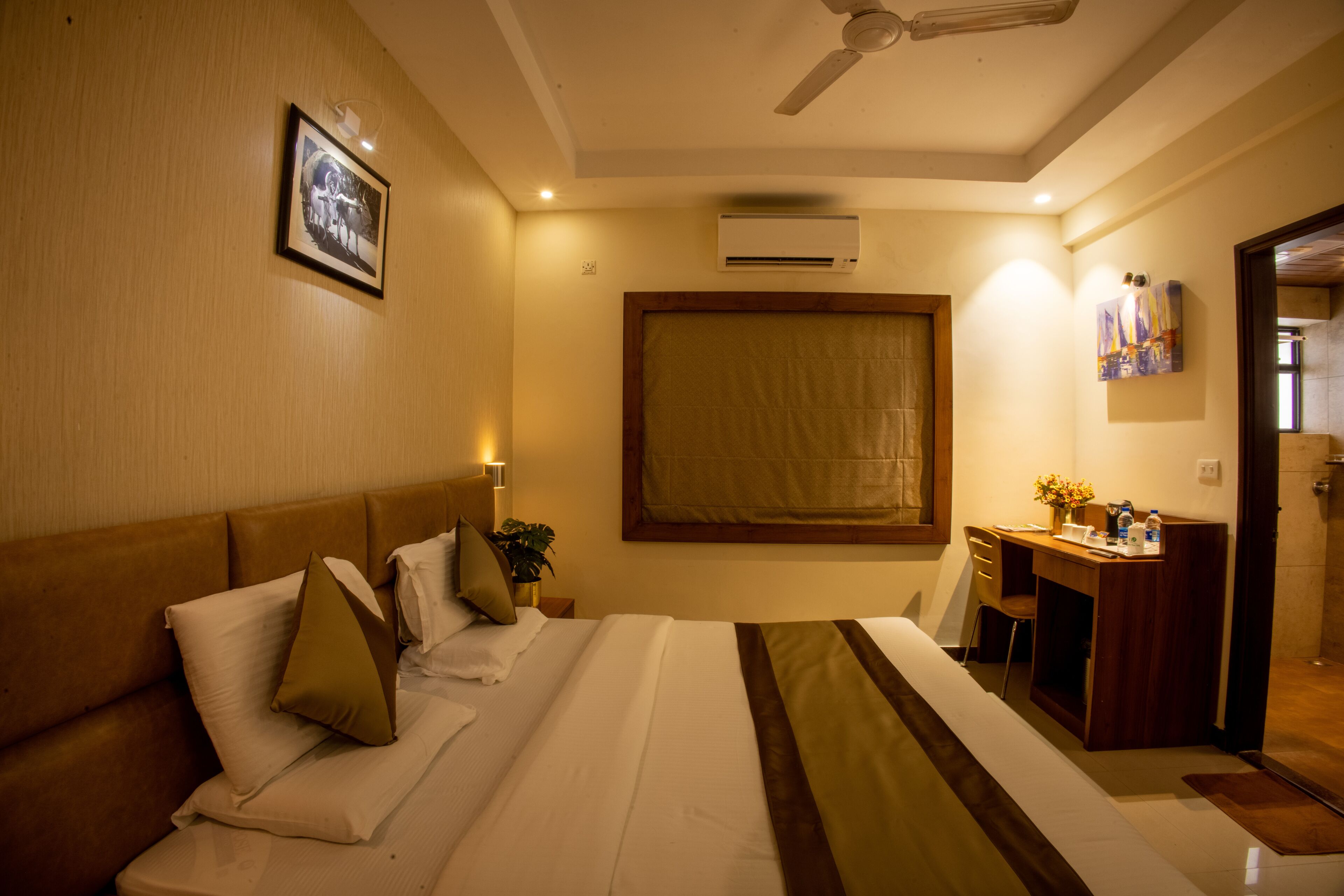 Una habitación de hotel con cama, escritorio, silla, ventilador de techo y aire acondicionado.