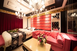 A hotel room with a red upholstered headboard, a pink sofa, a bed with a patterned bedspread, and a chandelier. - Hotel Secret Veny - Adults Only (Tokyo)