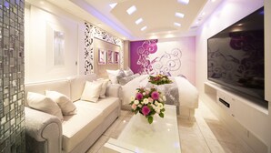 Uma sala de estar moderna com um sofá, uma mesa de centro com flores, uma TV de tela plana e arte decorativa nas paredes.