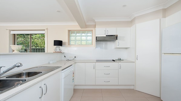 Una cocina moderna con armarios blancos, un lavamanos de acero inoxidable y una ventana con vistas a la vegetación.