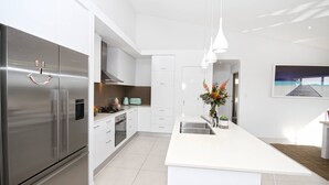 A modern kitchen with stainless steel appliances, white cabinetry, and pendant lighting. - Stunning Home With Spectacular Views (Coolum Beach)