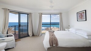 Un dormitorio con una cama grande, vistas al mar y un balcón con una silla.