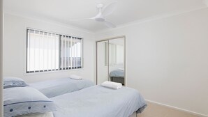 Un dormitorio con dos camas, un ventilador de techo, un ventanal con persianas y un espejo.