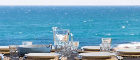 Una mesa dispuesta con platos, cubiertos y vasos, con vista al océano.